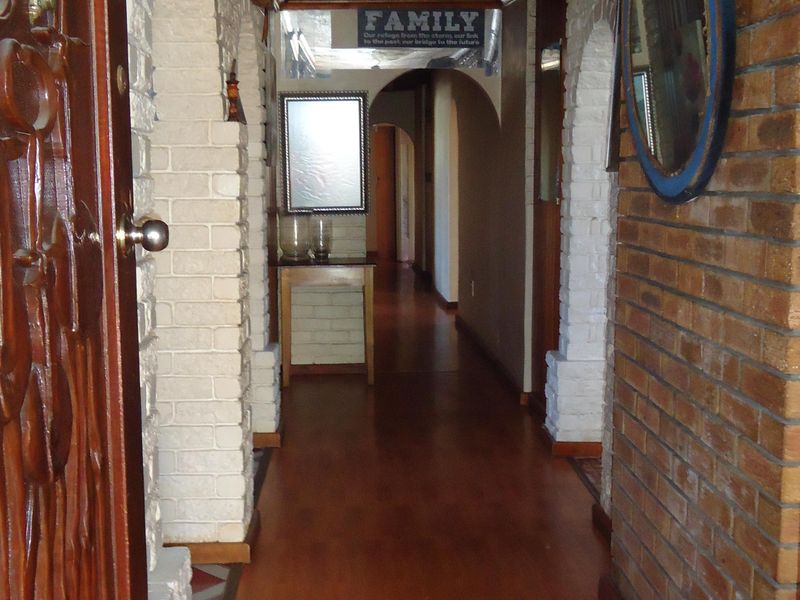 A hallway featuring exposed brick walls, arched architectural details, laminate flooring, and a timber-paneled ceiling.