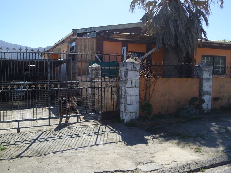 Front exterior view of a residential property featuring a metal security gate, masonry boundary wall, and a covered carport area.