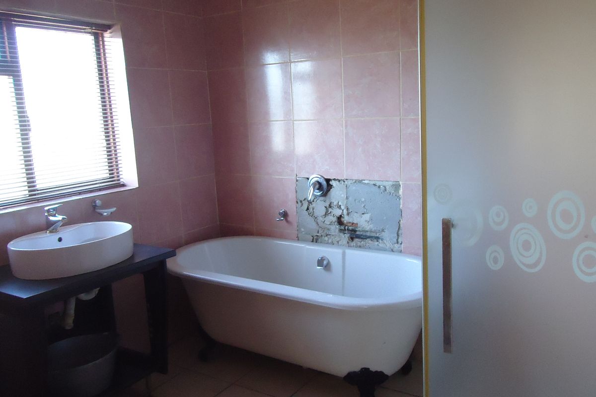 A bathroom featuring a freestanding bathtub, vessel sink, and shower enclosure, currently requiring repair to the tiled wall area behind the tub.