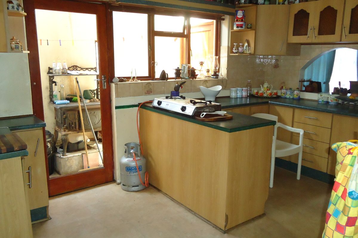 A dated kitchen featuring laminate cabinetry, a gas hob, and direct access to an adjacent utility area through a timber-framed door.