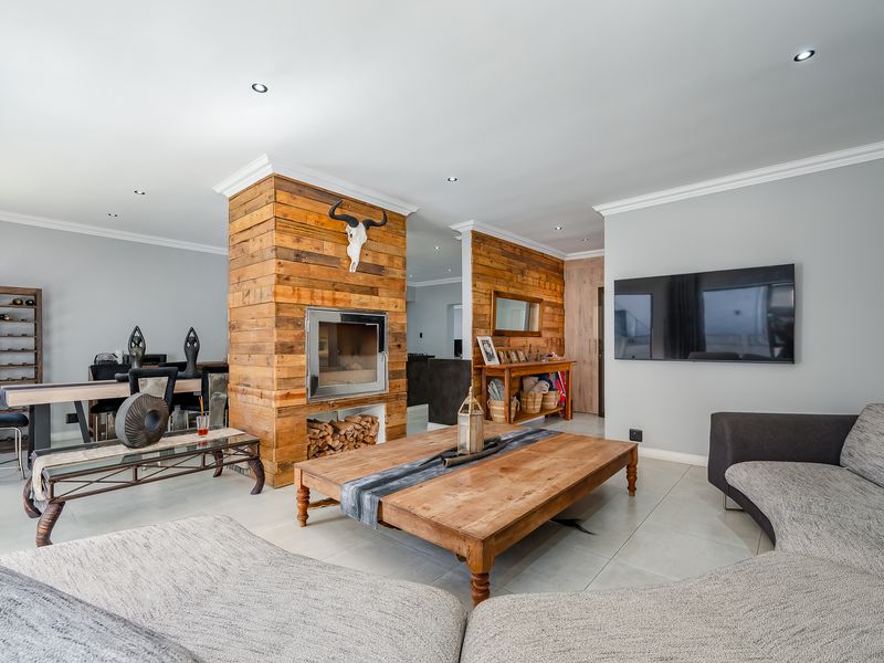 Spacious open-plan living area featuring a central timber-clad fireplace, tiled flooring, and recessed lighting, creating a warm and inviting atmosphere.