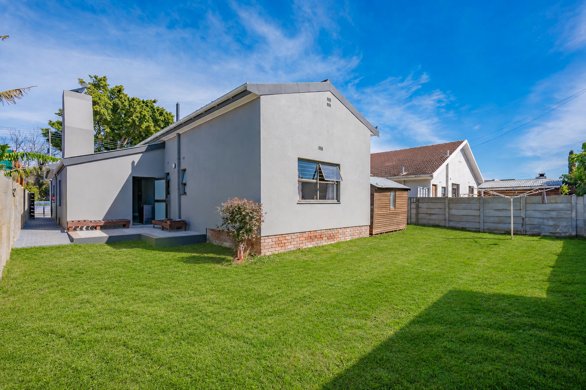 Rear view of the property featuring a well-maintained lawn, paved patio area, and a clean plastered exterior finish with a brick plinth.