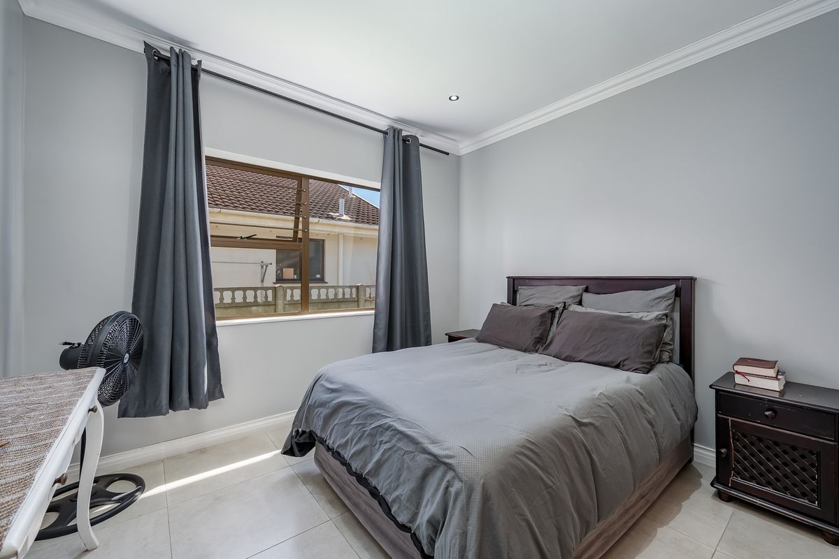 A well-maintained bedroom featuring neutral wall tones, tiled flooring, decorative cornicing, and recessed lighting, offering a clean and comfortable living space.