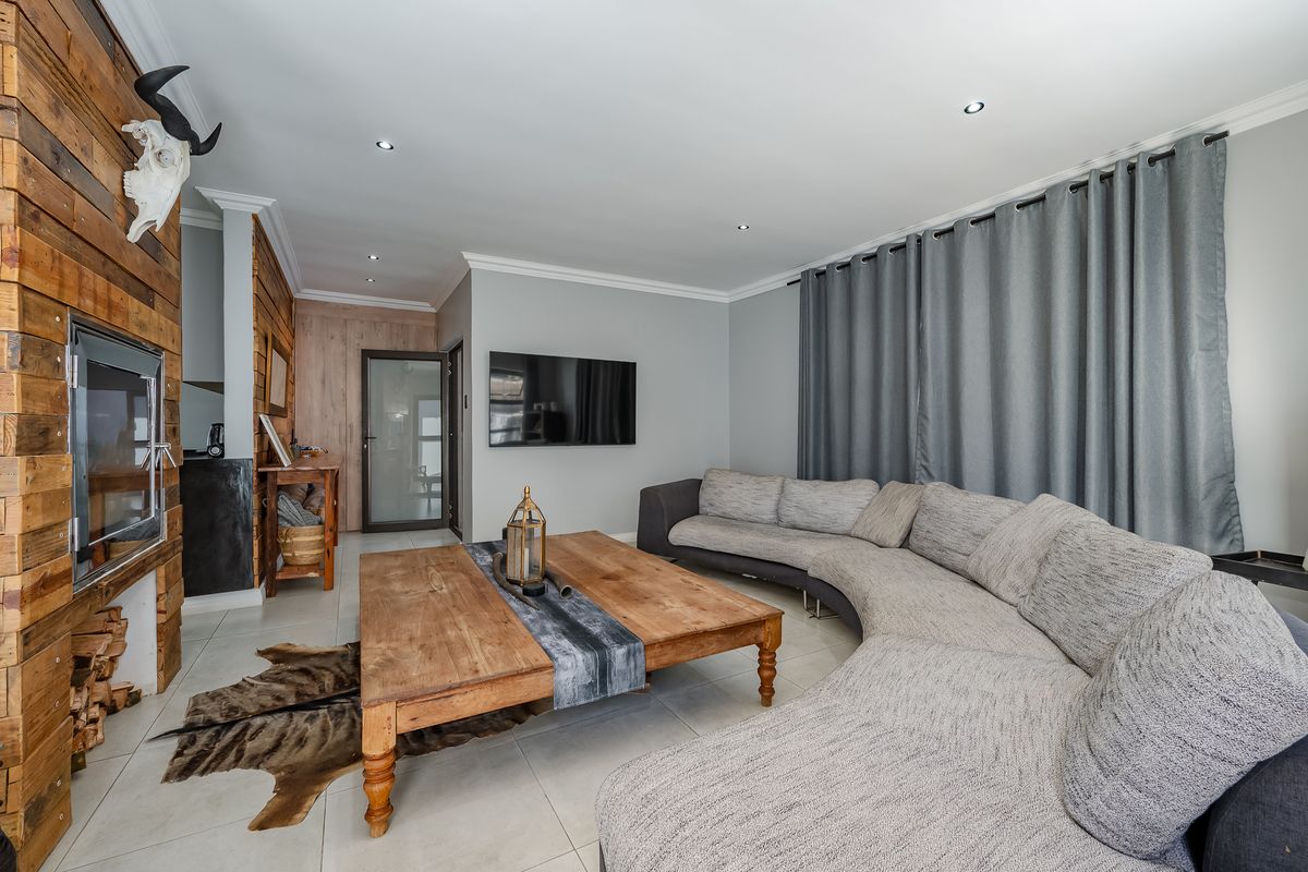 A modern living room featuring a striking timber-clad fireplace wall, tiled flooring, and recessed downlights, creating a warm and inviting atmosphere.