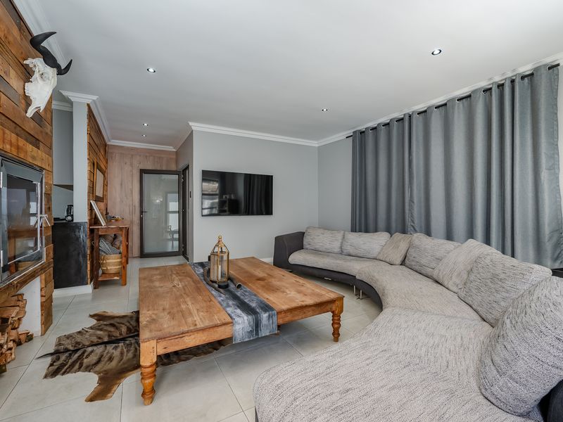 A modern living room featuring a striking timber-clad fireplace wall, tiled flooring, and recessed downlights, creating a warm and inviting atmosphere.