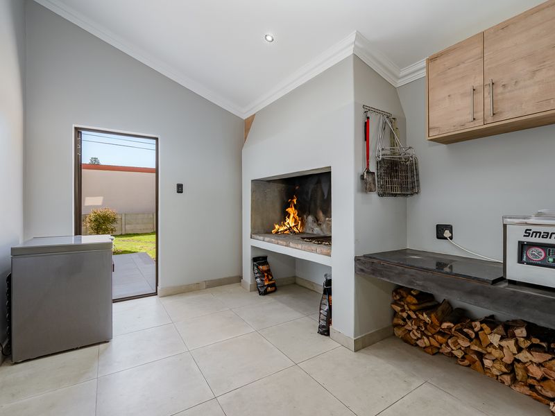 Covered patio area featuring a built-in braai, concrete prep counter, wall-mounted storage cabinetry, and direct access to the rear garden.