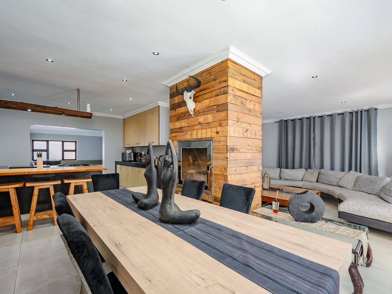 Spacious open-plan living and dining area featuring a central wood-clad fireplace, modern kitchen cabinetry, and tiled flooring throughout.