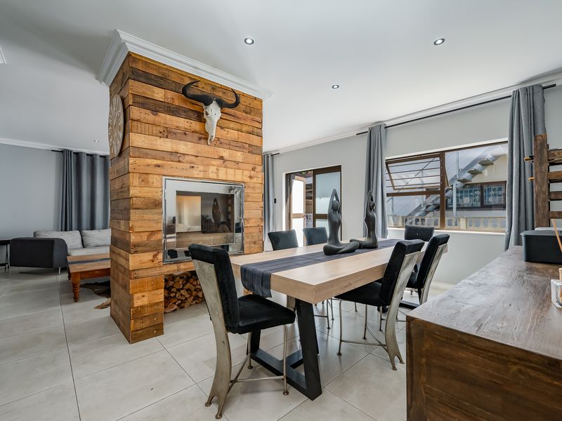 Spacious open-plan living and dining area featuring a prominent wood-clad built-in fireplace, tiled flooring, and modern recessed lighting.