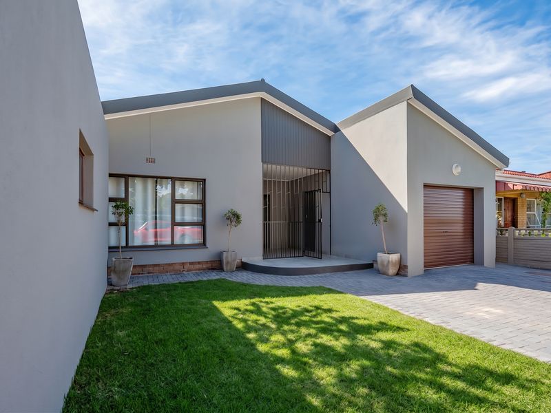 Modern front facade featuring a paved driveway, single garage, and well-maintained lawn with secure entrance gate.