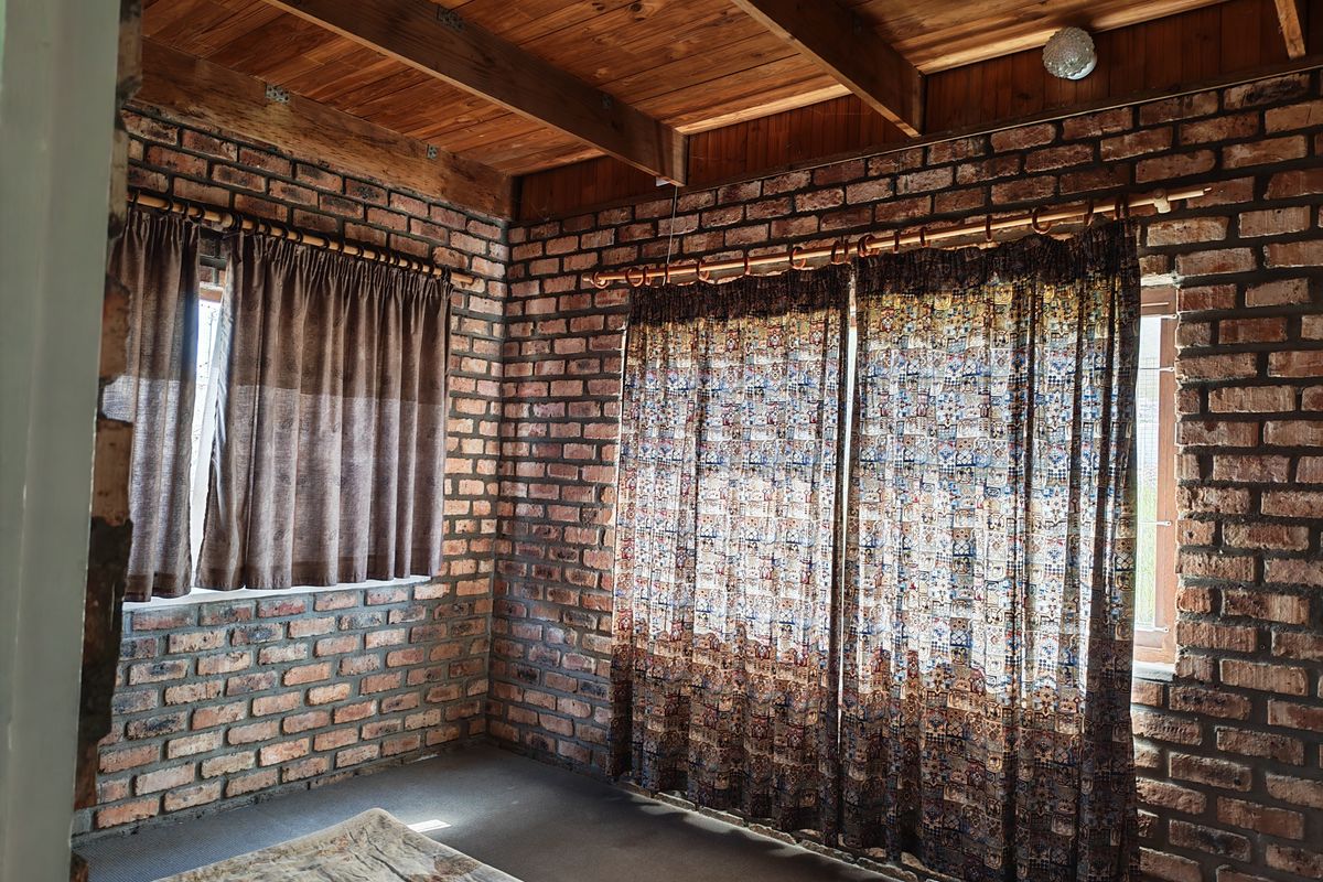 A rustic bedroom featuring exposed brick walls and a warm timber beam ceiling, offering a unique character-filled space with natural light.