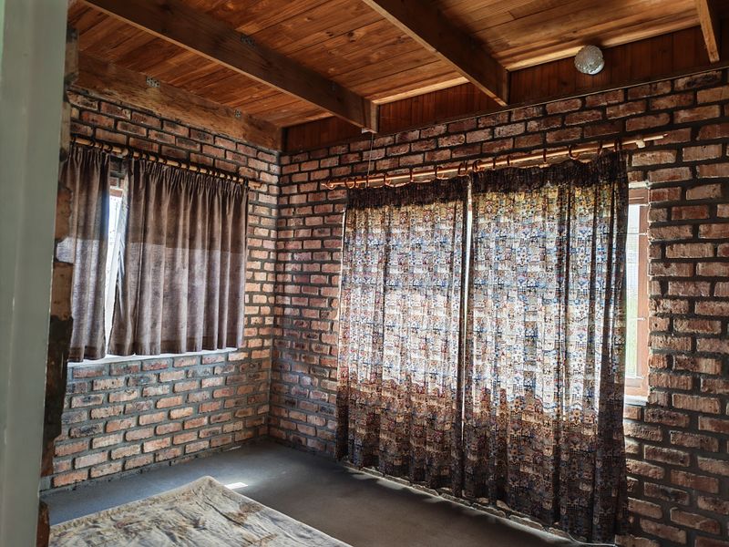 A rustic bedroom featuring exposed brick walls and a warm timber beam ceiling, offering a unique character-filled space with natural light.