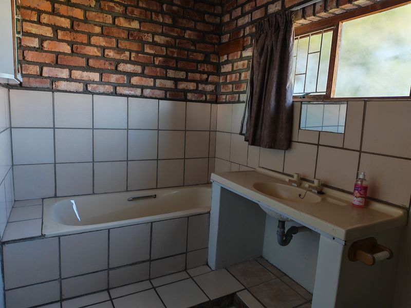 A dated bathroom featuring an exposed brick wall, built-in bathtub, and a vanity basin with exposed plumbing.