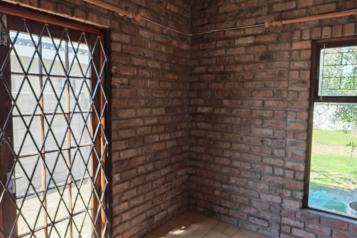 An empty room featuring exposed brick walls, tiled flooring, and a security gate leading to the exterior.