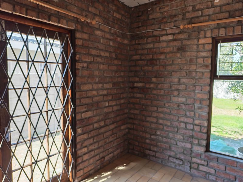 An empty room featuring exposed brick walls, tiled flooring, and a security gate leading to the exterior.