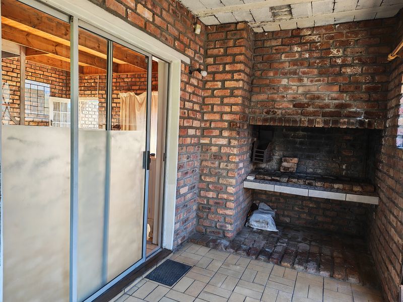 Covered patio area featuring a built-in brick braai, tiled flooring, and sliding glass door access to the interior.