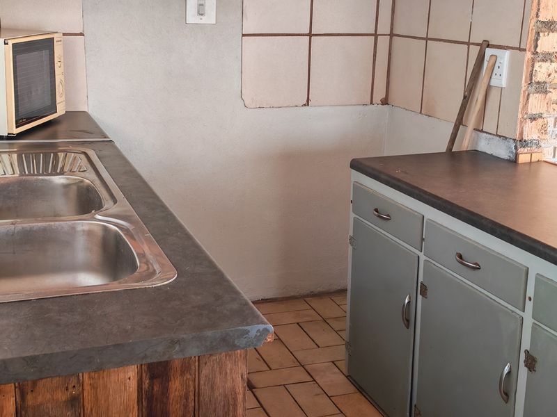A dated kitchen area featuring a double stainless steel sink, laminate countertops, tiled backsplash, and original built-in cabinetry with tiled flooring.
