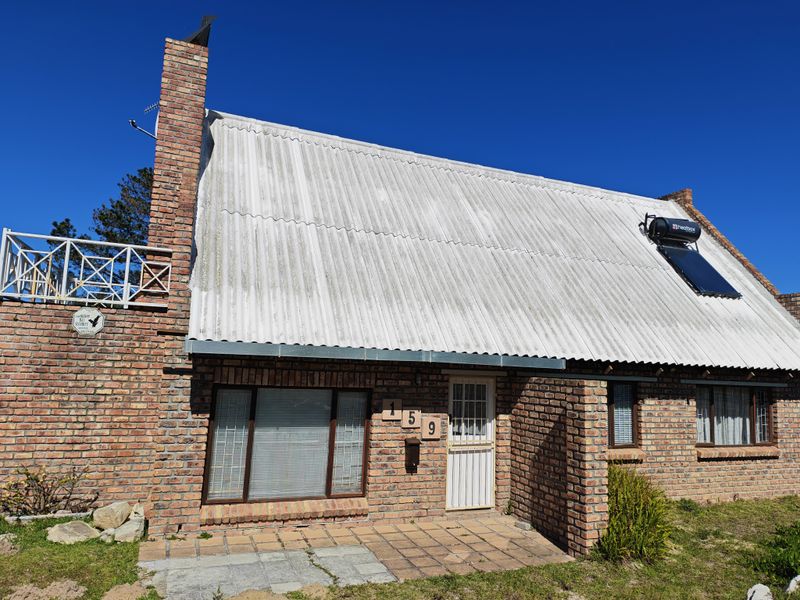 Front elevation of a brick house featuring a corrugated roof, solar water heating system, brick chimney, and a small paved entrance area.
