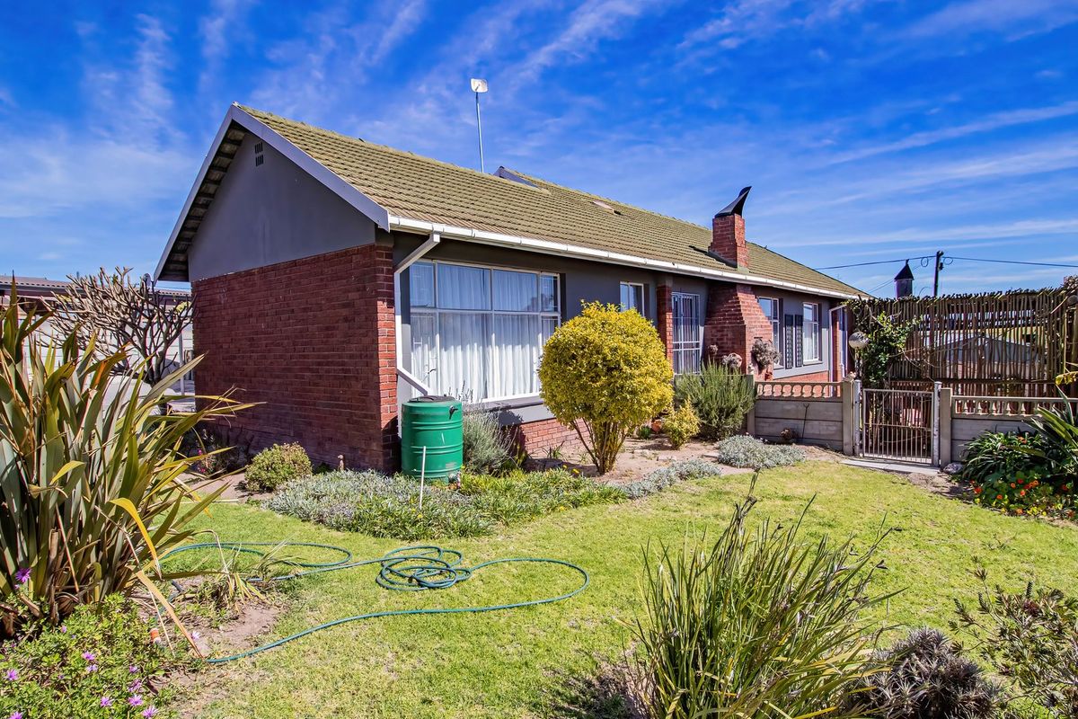 Rear view of a brick house featuring a tiled roof, chimney, and a landscaped garden with a rainwater tank and secure fencing.