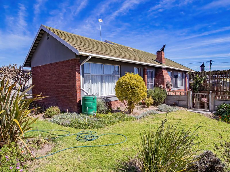 Rear view of a brick house featuring a tiled roof, chimney, and a landscaped garden with a rainwater tank and secure fencing.