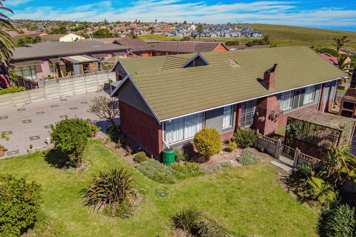 Aerial view of a residential property featuring a tiled roof, brick chimney, paved driveway, and a built-in outdoor braai area in the garden.