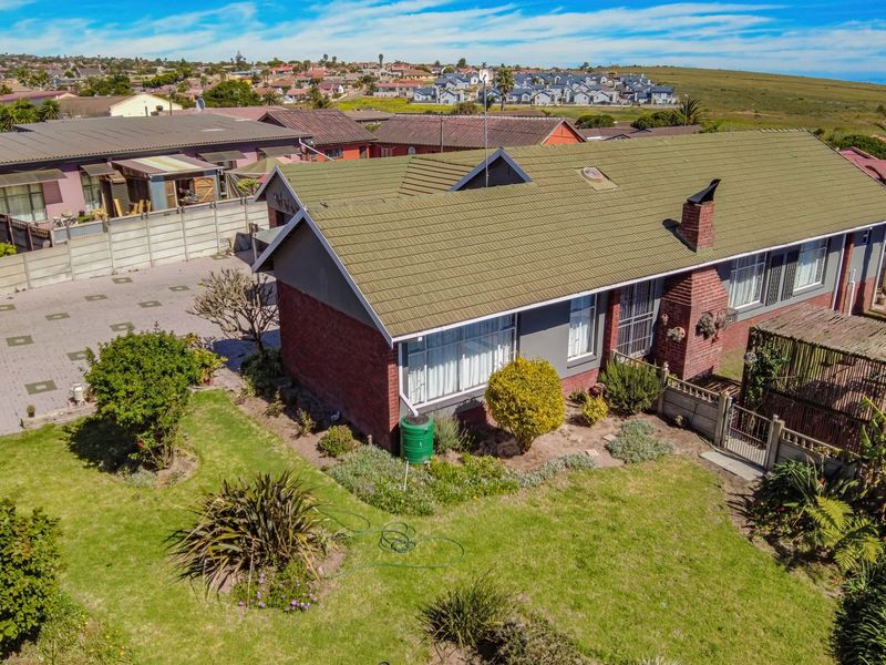 Aerial view of a residential property featuring a tiled roof, brick chimney, paved driveway, and a built-in outdoor braai area in the garden.