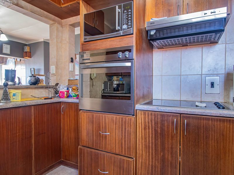 A functional kitchen featuring wood-finish cabinetry, built-in oven and microwave, extractor fan, and tiled backsplash with a breakfast bar overlooking the living area.