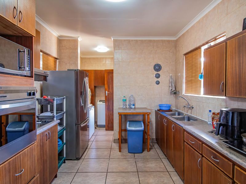 A functional kitchen featuring wood-finish cabinetry, built-in oven and microwave, double sink, and tiled surfaces throughout.