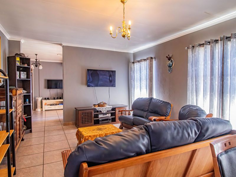 A spacious living room featuring neutral wall tones, tiled flooring, and a classic chandelier, offering a comfortable and functional layout.