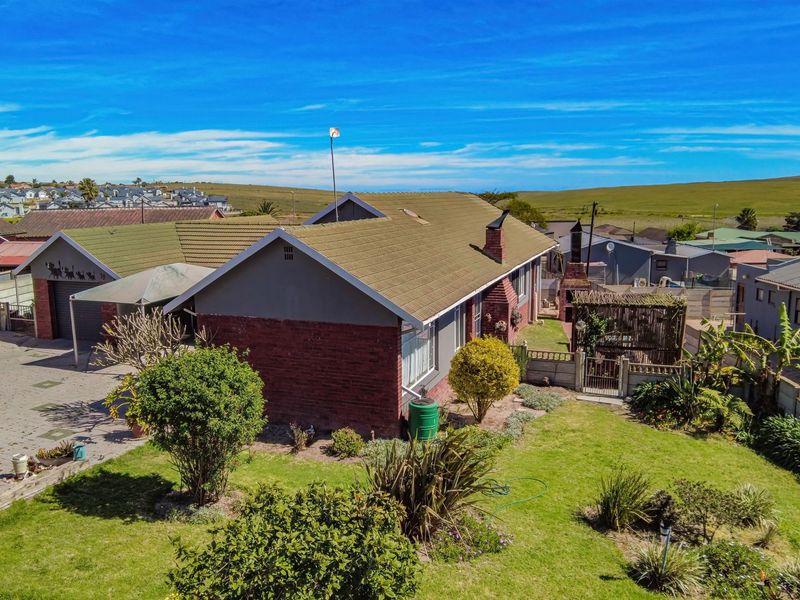 Aerial view of a residential property featuring a brick facade, tiled roof, paved driveway, garage, and a landscaped garden with a built-in braai area.