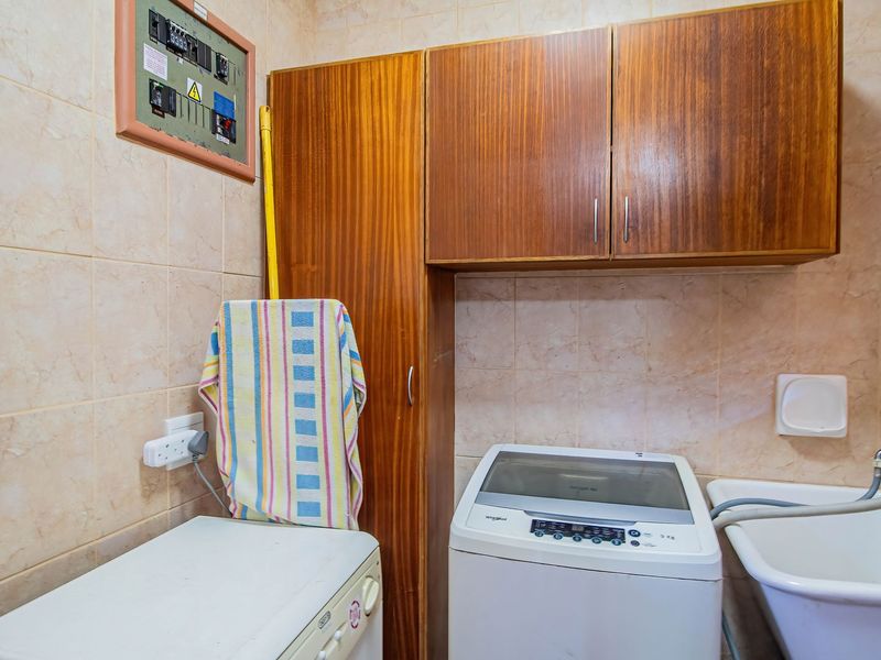 A functional laundry room featuring tiled walls, built-in wooden cabinetry, a utility sink, and an integrated electrical distribution board.