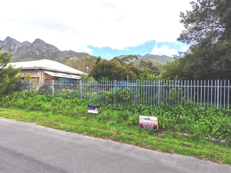 Street view of the property featuring a brick house, steel palisade fencing, and mountain views in the background.