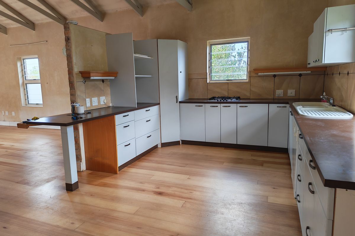 A spacious kitchen featuring built-in cabinetry, a gas hob, and exposed timber rafters, offering a functional layout with potential for modern updates.
