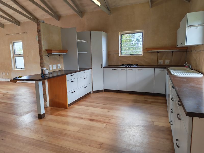 A spacious kitchen featuring built-in cabinetry, a gas hob, and exposed timber rafters, offering a functional layout with potential for modern updates.