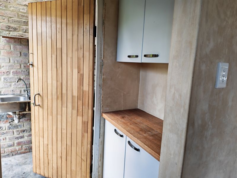 A functional scullery or utility area featuring built-in cabinetry, a wooden countertop, and an exposed brick wall with a stainless steel sink.