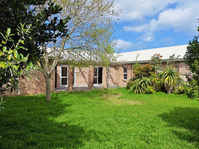 A rear view of the house featuring a face brick facade, a paved patio area, and a well-maintained garden with mature trees.