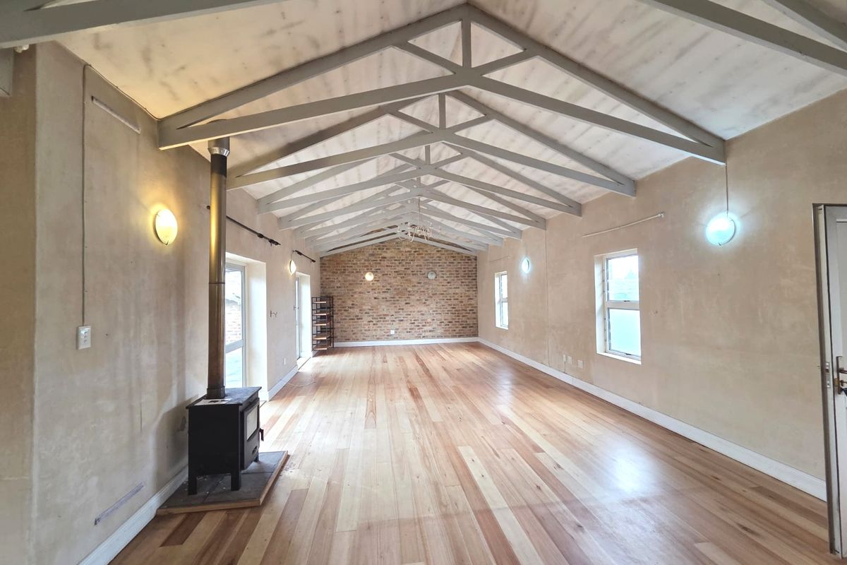 Spacious living area featuring high vaulted ceilings with exposed trusses, a wood-burning stove, polished timber flooring, and a rustic exposed brick feature wall.