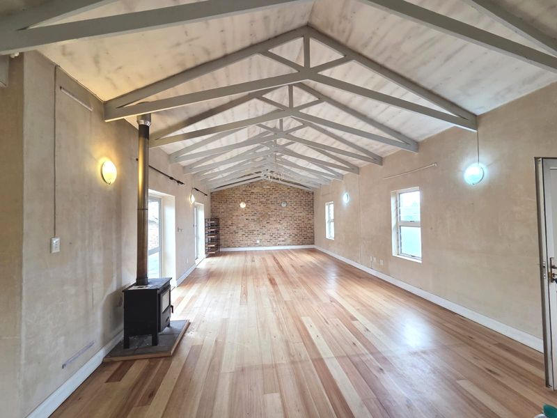 Spacious living area featuring high vaulted ceilings with exposed trusses, a wood-burning stove, polished timber flooring, and a rustic exposed brick feature wall.