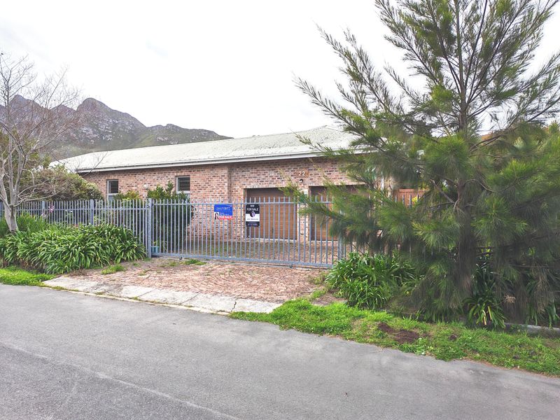 Front exterior view of a single-story brick house featuring a double garage, metal roof, and secure steel gate access from the street.