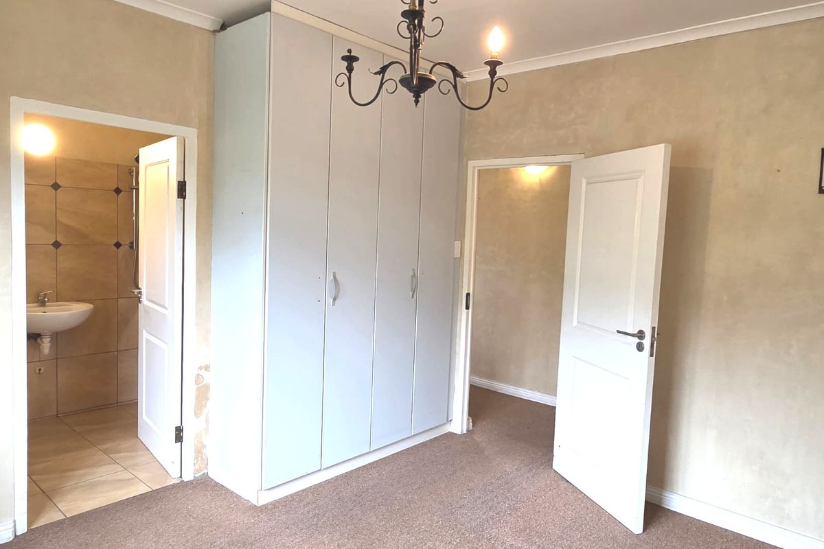 A bedroom featuring built-in wardrobes, carpet flooring, and an en-suite bathroom, requiring cosmetic updates to the walls and flooring.