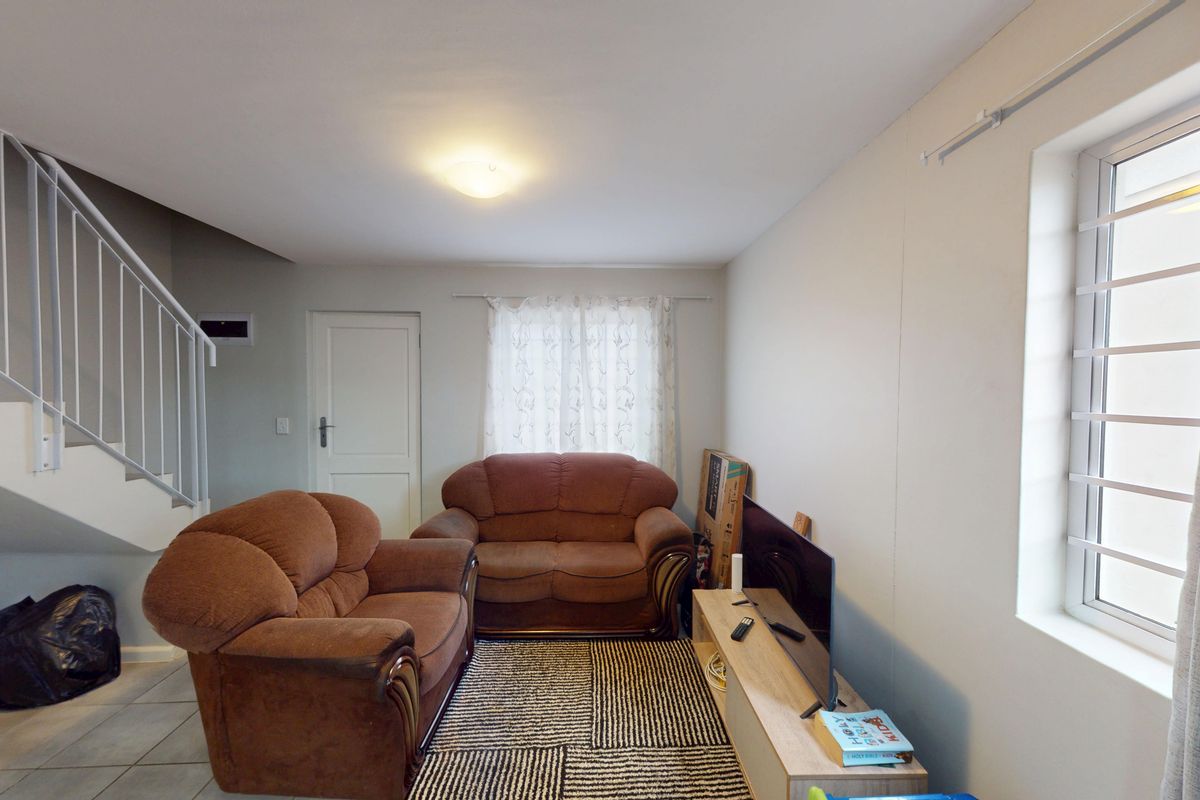A functional living room featuring tiled flooring, a staircase with a metal balustrade, and a window fitted with security bars.