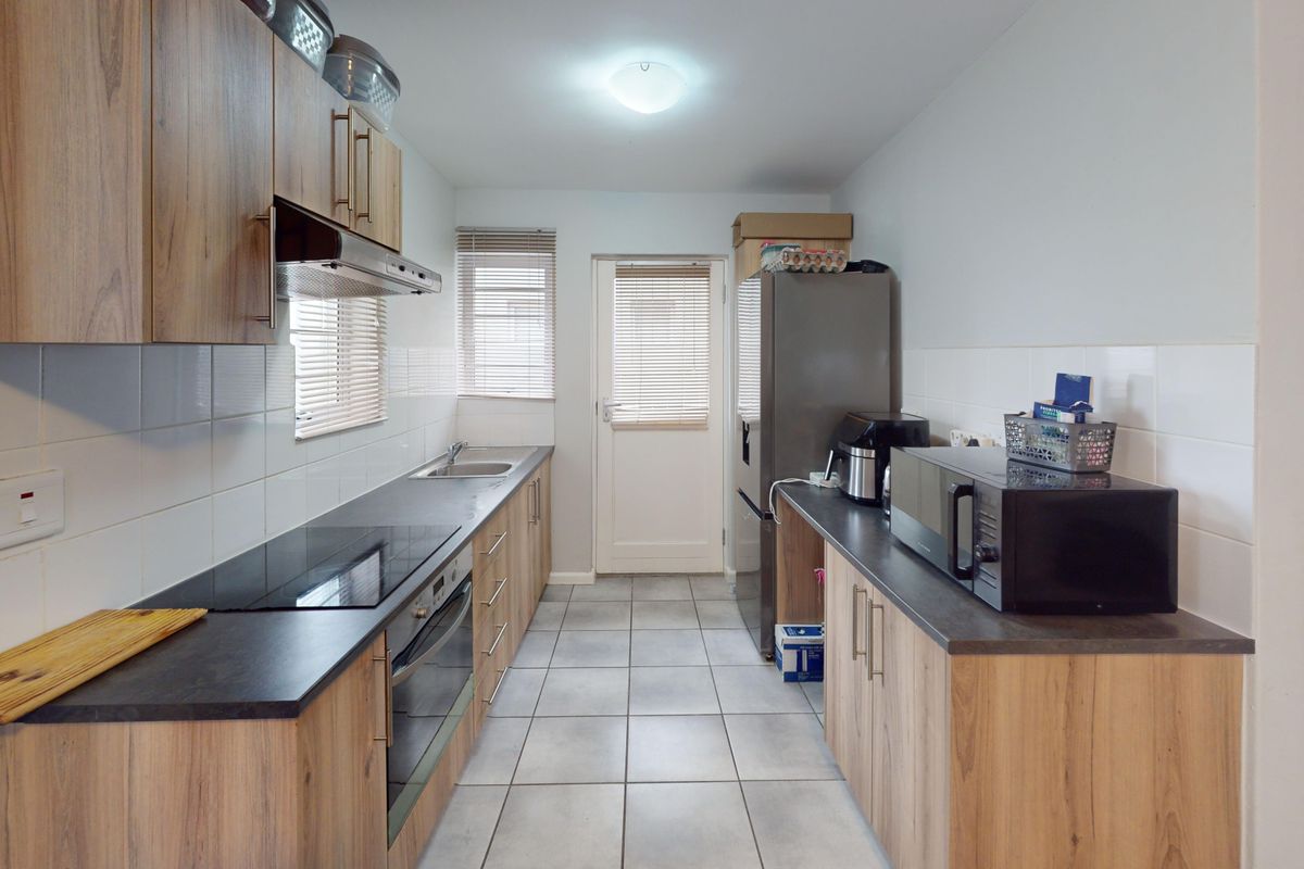 A functional galley-style kitchen featuring wood-look cabinetry, dark countertops, integrated oven and hob, and tiled flooring with direct access to the exterior.