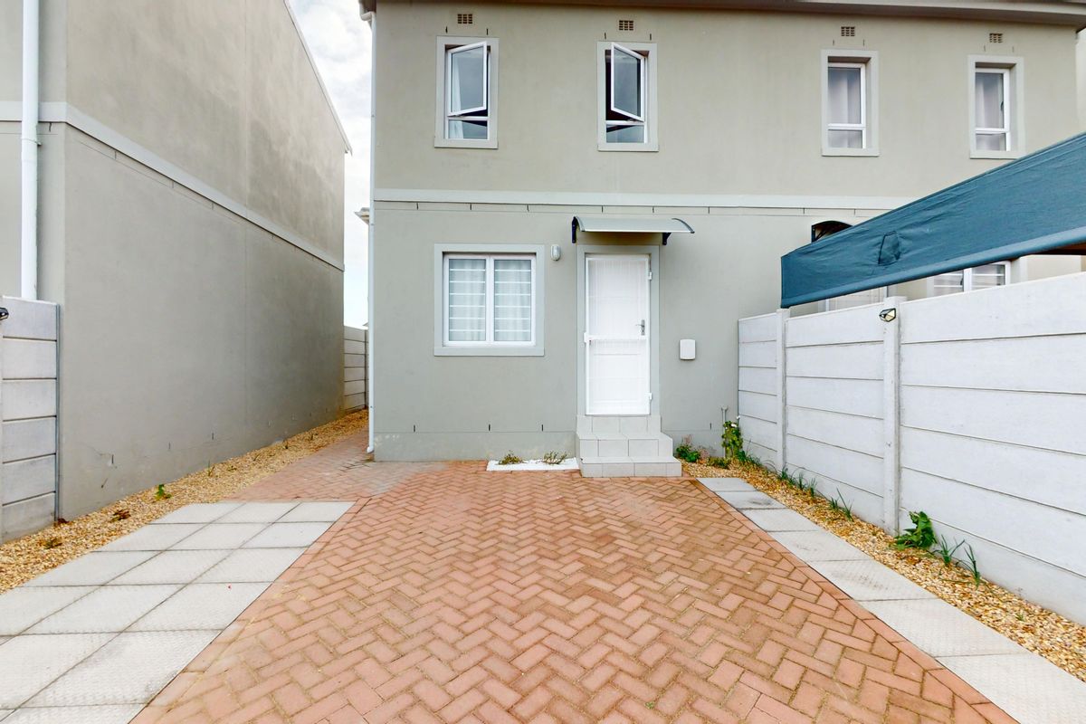 Rear exterior view of a two-story house featuring a paved courtyard, precast boundary walls, and a small entrance area with an awning.