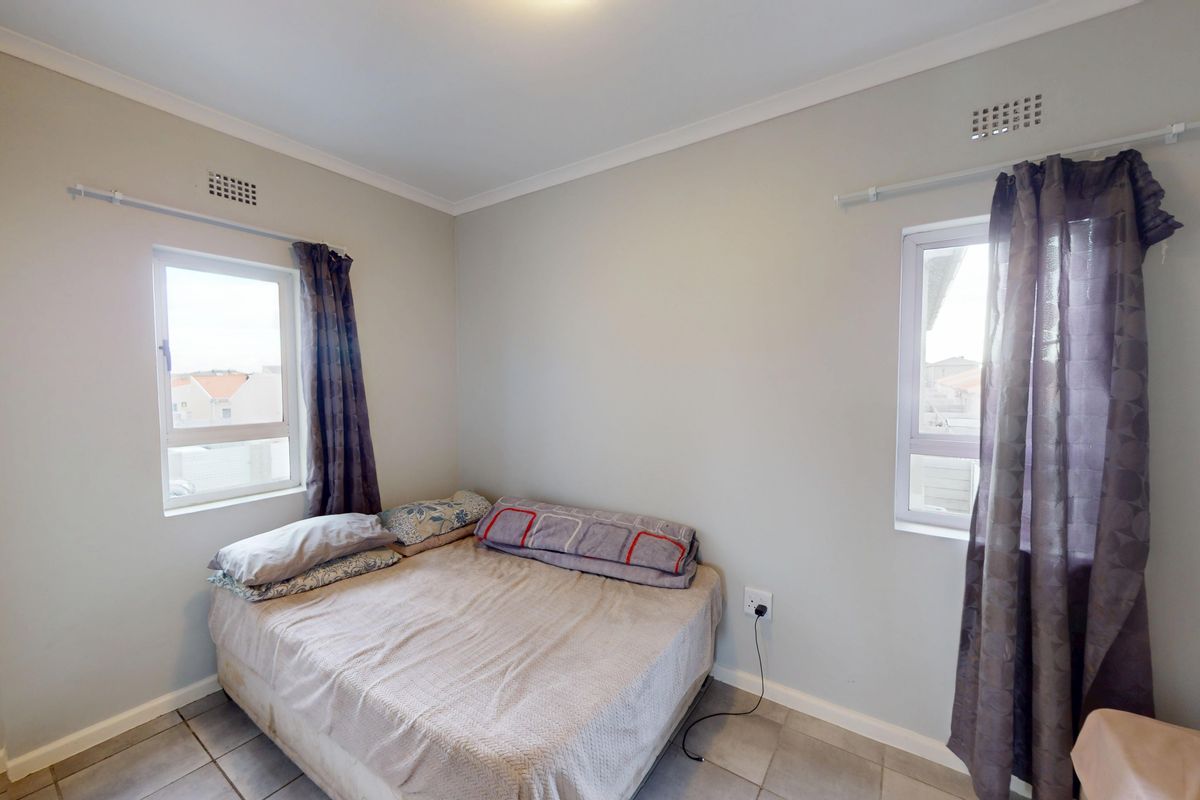 A functional bedroom featuring tiled flooring, dual windows with curtain rods, and integrated ventilation vents, providing a neutral space ready for personalization.