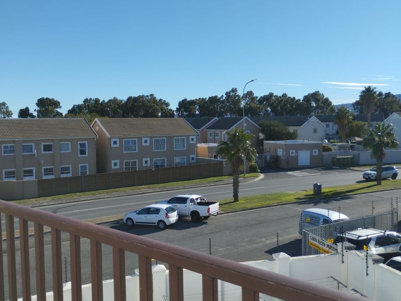 An elevated view from a balcony overlooking a suburban street, surrounding residential apartment blocks, and local infrastructure.