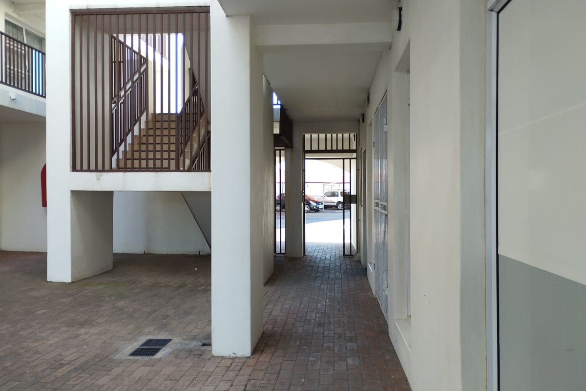 An outdoor common area featuring brick paving, a metal staircase, and security gates within an apartment complex.