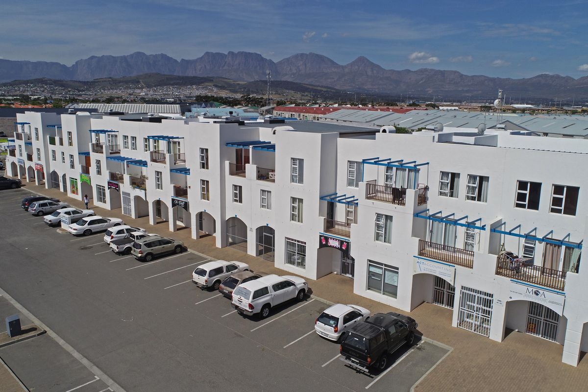 Aerial view of a multi-story apartment complex featuring white facades, private balconies, and dedicated ground-level parking bays.