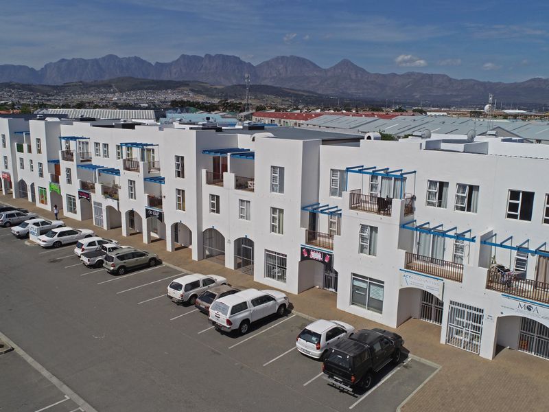 Aerial view of a multi-story apartment complex featuring white facades, private balconies, and dedicated ground-level parking bays.