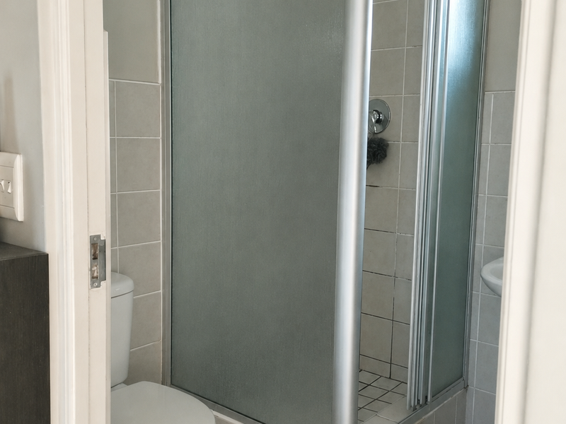 A functional bathroom featuring a corner shower enclosure, tiled walls and flooring, and a standard toilet.