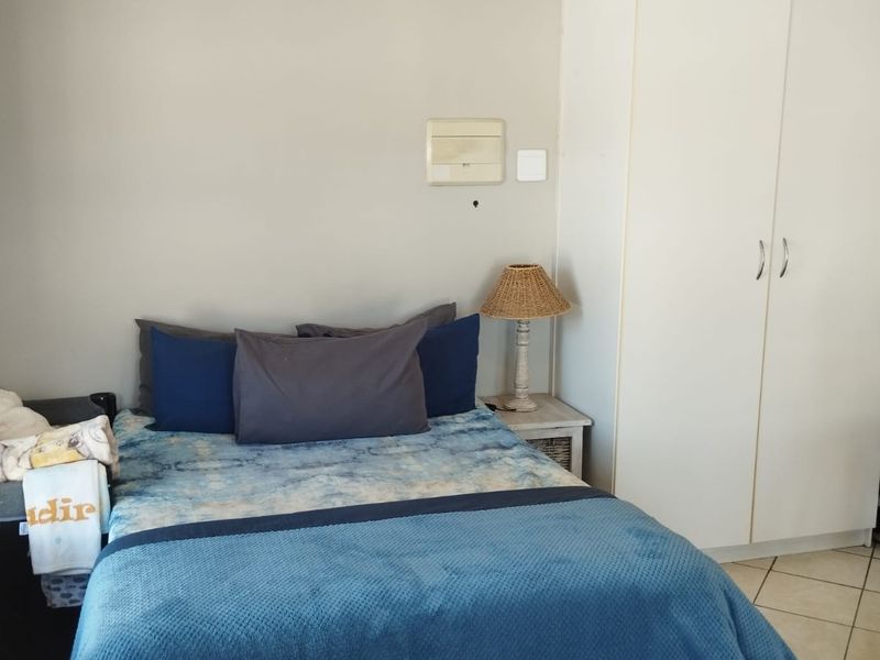 A functional bedroom featuring tiled flooring, a built-in white wardrobe, and neutral wall finishes, providing a clean and practical living space.