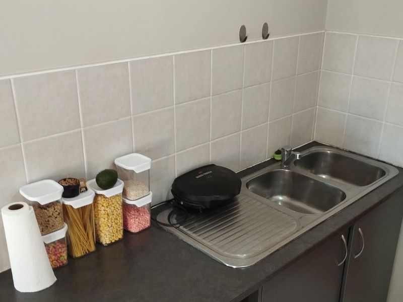 A compact kitchen area featuring a double bowl stainless steel sink, dark laminate countertops, and a neutral tiled backsplash.